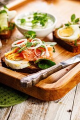 Appetizing canapes or sandwiches with smoked salmon. Toast with salted fish, cheese, egg, onion rings and fresh salad. Delicious breakfast or snack on a wooden tray. Vertical shot. Copy space
