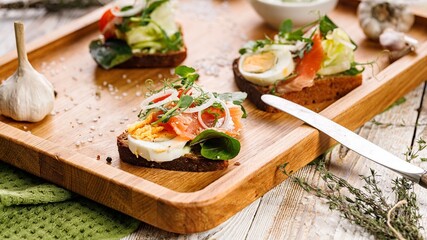 Appetizing canapes or sandwiches with smoked salmon. Toast with fish, soft cheese, eggs, onion rings and salad. Traditional Delicious breakfast or snack on a wooden tray. Food still life. Close-up