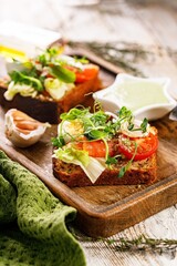 Close-up toast with salted fish, cheese, egg, onion rings and salad. Appetizing canapes or sandwiches with smoked salmon. Traditional Delicious breakfast or snack on a wooden background Vertical shot