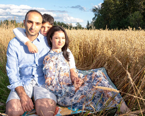 Family on vacation outside the city. A man, a woman and a child hug and have a picnic in the ears of wheat.