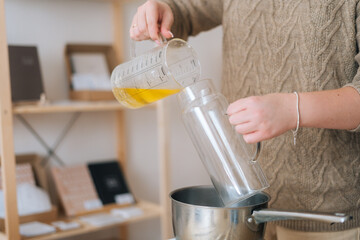 Close-up cropped shot of unrecognizable female artisan pouring melted wax into glass vessel for...