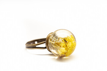 Natural dried plants inside epoxy resin ring. Sphere shaped mold, brass colored metal base, yellow flowers. Selective focus on the details, object isolated on white background.