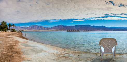 Fototapeta na wymiar Resting chair on stone pier at a shore of the Red Sea, at the distance seen marine port of Aqaba in Jordan