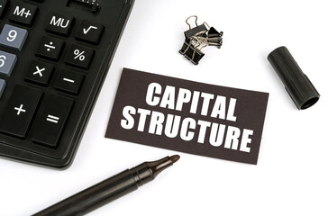 On a white table there is a calculator, a marker and a black plate with the inscription - Capital...