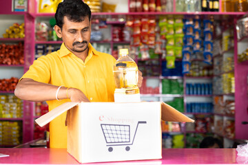 Grocery or kirana store shopkeeper packing groceries on e-commerce shopping box at retail store -...