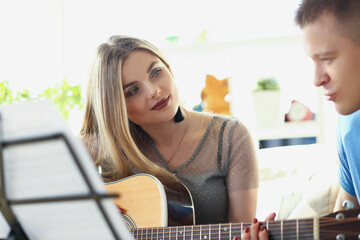Woman teaching man how to play on guitar instrument, music class at home