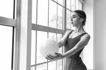 Black and white portrait of beautiful young gymnast with ball in gym
