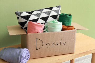 Cardboard box with donations on bench against green background
