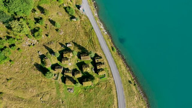 Grass roof house cluster on a meadow near a lake from above