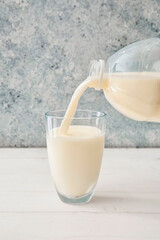 Pouring milk from gallon container into glass on table