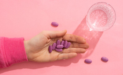 handful of tablets in the palm of your hand next to a glass of water