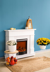 Stylish fireplace with autumn decor near blue wall in room