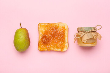 Glass jar of tasty pear jam and bread on pink background