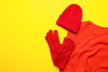 Warm hat, gloves and sweater on yellow background