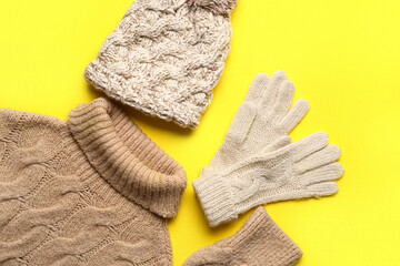 Warm hat, gloves and sweater on yellow background, closeup