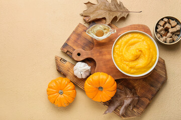 Bowl of tasty pumpkin cream soup and bread on beige background