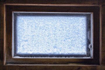 Close-up of a small window covered with crystals of ice frost. Light shines through a frozen snow-covered wooden window on a chilly day. Background from small fluffy ice crystals on the window.