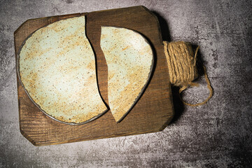 A handmade ceramic plate, broken in half, lies on a wooden board on a gray background. Deconstruction concept, top view, close-up.