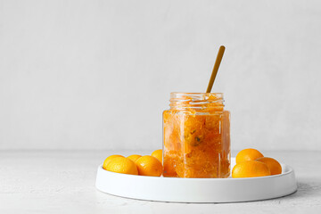 Jar of tasty kumquat jam and fresh fruits on light background
