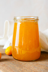 Jar of tasty kumquat jam on light background