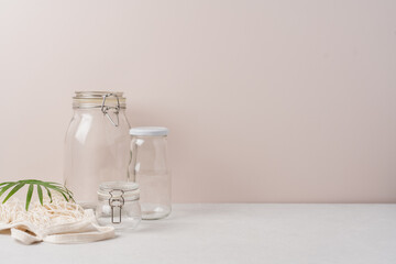 Set of glass jars and bags for zero waste grocery shopping. Eco friendly and reuse concept. Side view, light beige background