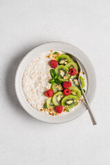 Oatmeal with kiwi and raspberries in ceramic bowl on light background with copy space. Healthy breakfast top view