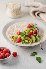Oatmeal with kiwi and raspberries in ceramic bowl on light background with copy space. Healthy breakfast side view