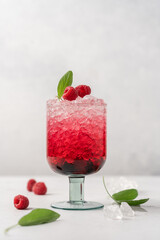 Glass of bright pink raspberry drink with crushed ice on light background. Refreshing berry summer drink