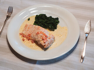 Salmon in Cream Sauce with Buttered Spinach on a White Plate with Silver Fish Knife and Fork