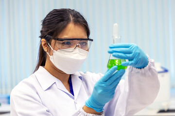 Woman scientist working in laboratory with Erlenmeyer flask with solutions in laboratory. Technician woman in medical coat uniform with protective goggles holding solvent liquid. Selective in face.