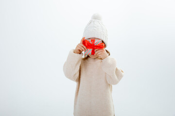a cute little girl smiling in a winter hat holding boxes of gifts isolated on a white background