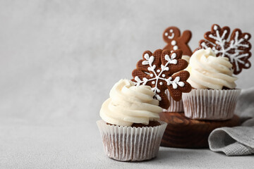 Tasty Christmas cupcakes with gingerbread cookies on light background
