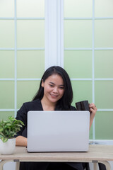 Woman sitting on chair with laptop at table holding drinking glass and looking at screen