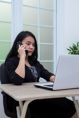 Business woman sitting on chair while making phone call in front of laptop with flat facial expression