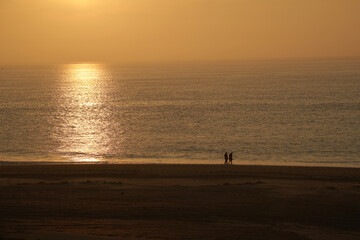 2 people walking on the North Sea beach in South Holland. Sunset over the orange shining sea. Togetherness.