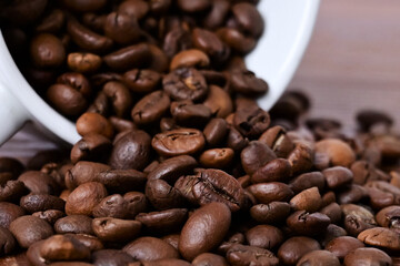 Naklejka premium Coffee beans spill out of a white cup onto a wooden table. Coffee beans on a wooden background. Close-up