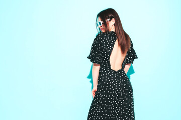 High fashion portrait of young beautiful brunette woman wearing nice trendy summer polka-dot dress.Sexy fashion model posing near blue wall in studio.Fashionable female with red lips
