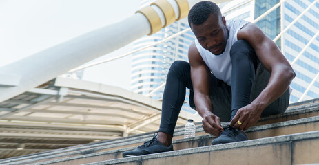 african american runner tying shoelaces of sneaker with water bottle in urban city outdoors
