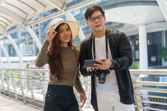 young Asian couple travelers using map application on smartphone . Lover tourists and luggage sightseeing in city and searching location on a mobile phone travel in vacation outdoors .
