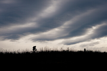 Obraz na płótnie Canvas Silhouette of a cyclist on a dike in stormy weather