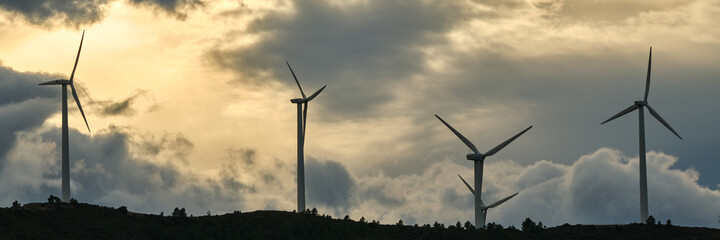 panoramic view of some wind turbines in a wind farm in the mountains at sunset. green ecological energy.