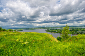 Fototapeta na wymiar Summer landscape, a large full-flowing river, meadow flowers on the banks of the river, mighty clouds in the sky, a tourist walk along the Kama River
