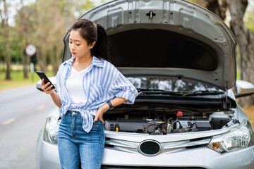 Beautiful asian woman sitting on a car broke down on the road. She trying to fix the problem and...