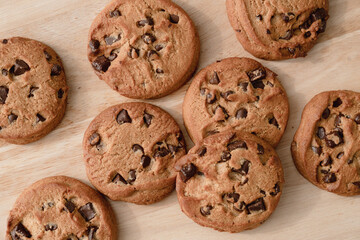 A lot of chocolate chip cookies piled up on a wooden plate.
