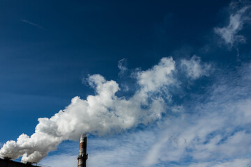 White and gray smoke and steam from a high concrete chimney against the bright blue sky