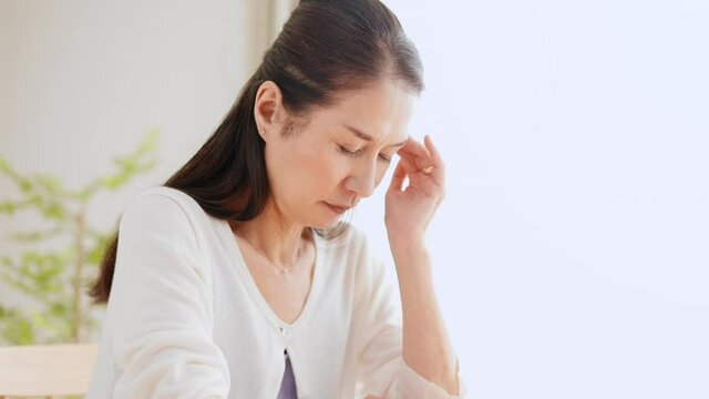 こめかみを押さえるシニア女性　頭痛