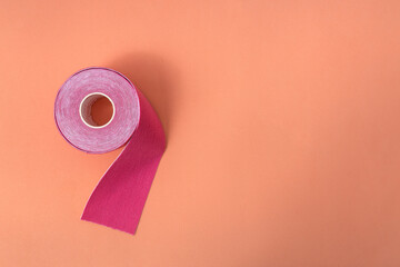 Top view of pink kinesiology tape and pink little scissors on the orange surface.Empty space - obrazy, fototapety, plakaty