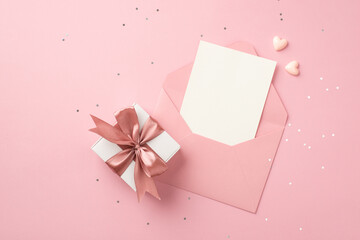 Top view photo of white giftbox with pink ribbon bow small hearts open pink envelope with paper...