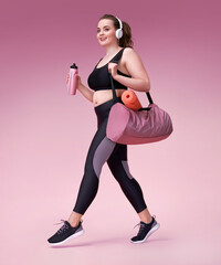 Go to training! Smiling sporty woman with sports bag and shaker. Photo of model with curvy figure in fashionable sportswear on pink background. Sports motivation and healthy lifestyle - obrazy, fototapety, plakaty