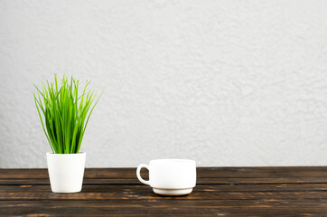 Green flowerpot. Sprout of greenery. The cup is on the table. Working wooden table.